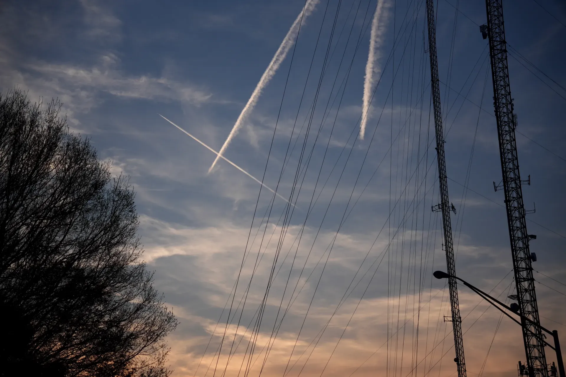 A radio tower with contrails at sunset.