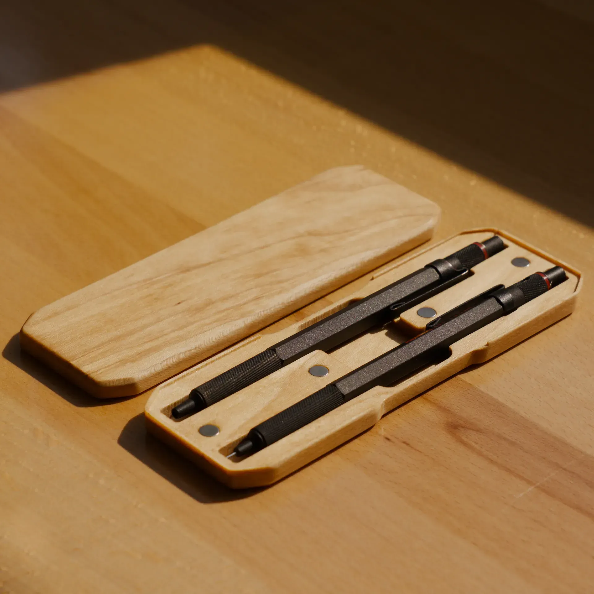 A machined wooden pencil case holding two pencils.